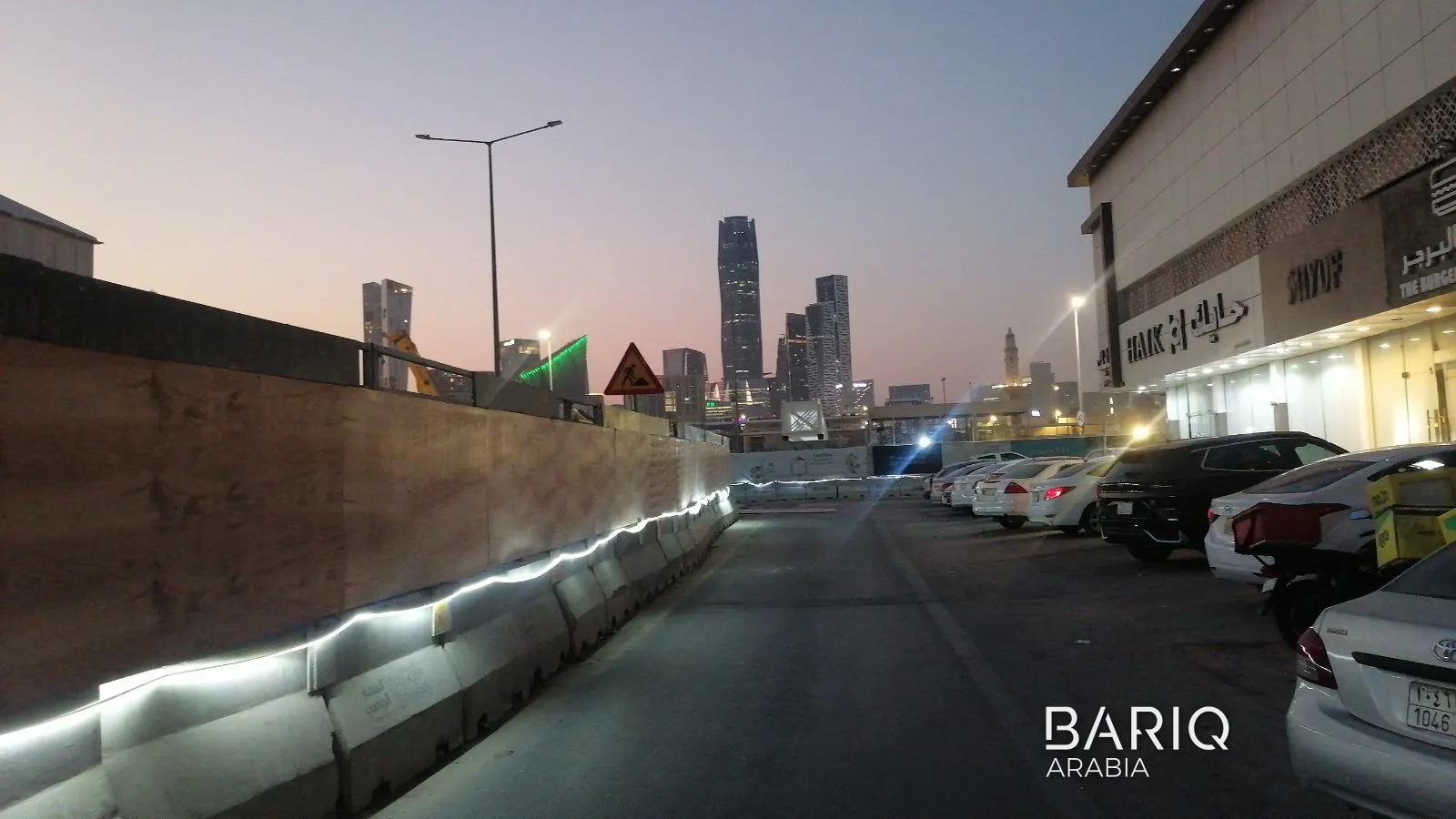 Lit hoarding and barriers beside the road on Sports Boulevard at night